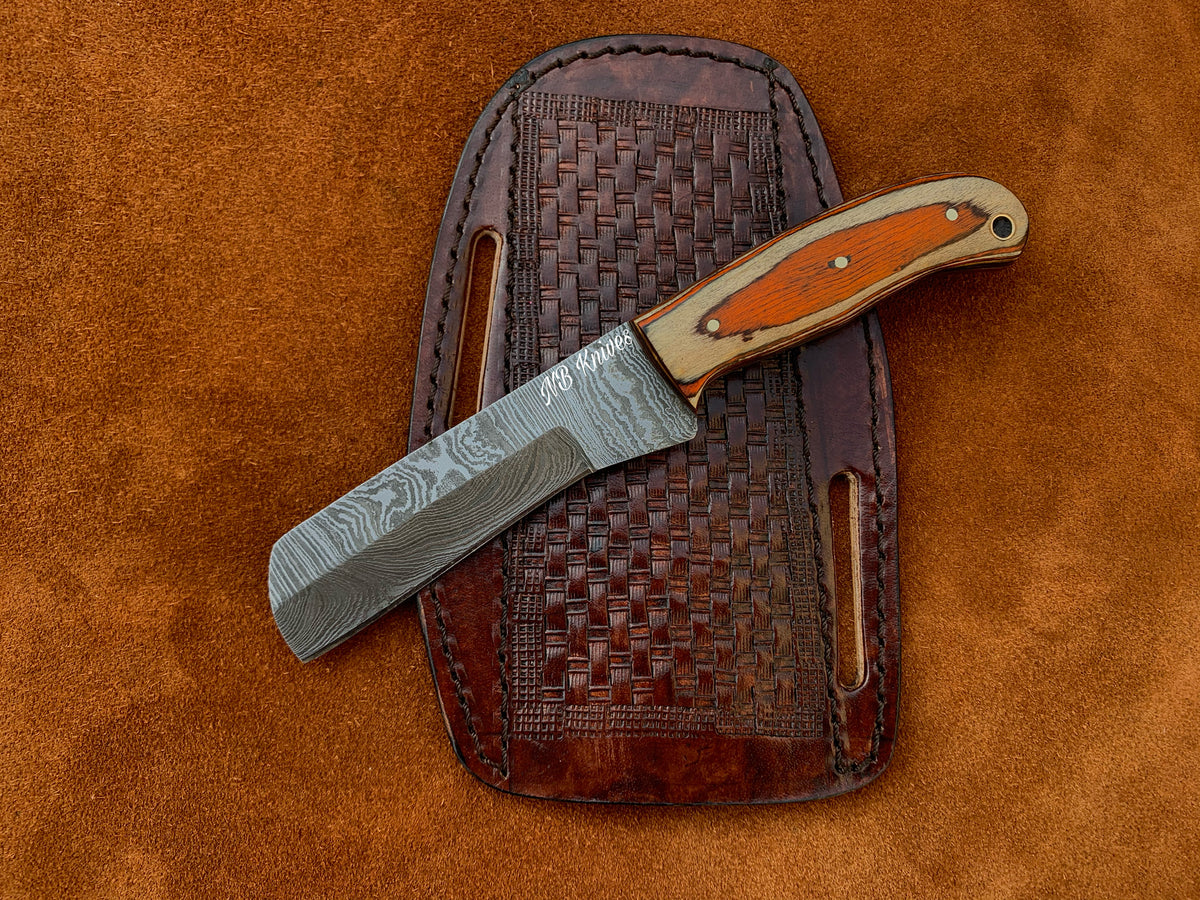 A handmade Damascus steel cowboy bull cutter knife with a brown leather sheath, featuring a patterned blade and a wooden handle.