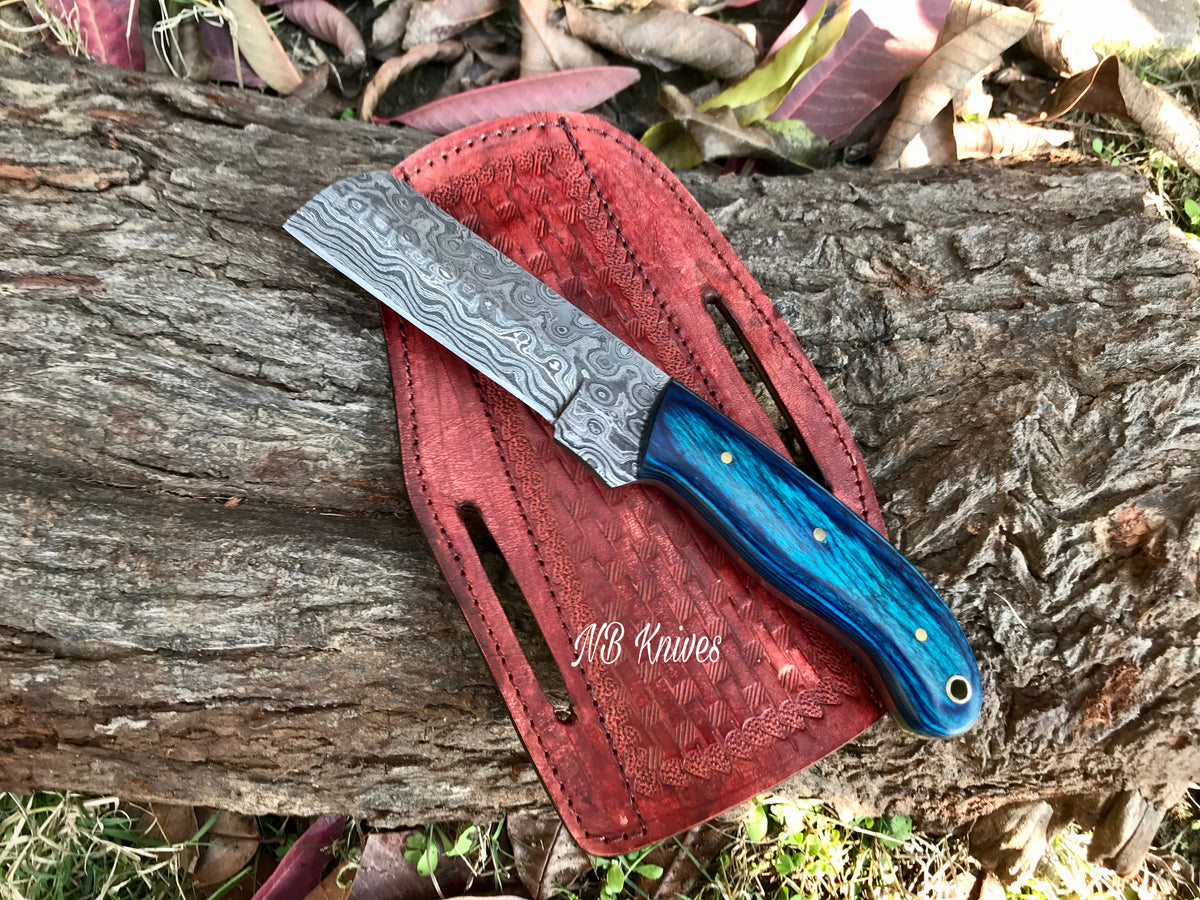 A custom handmade Damascus steel bull cutter knife with a patterned blade and blue wooden handle, displayed on a red leather sheath.