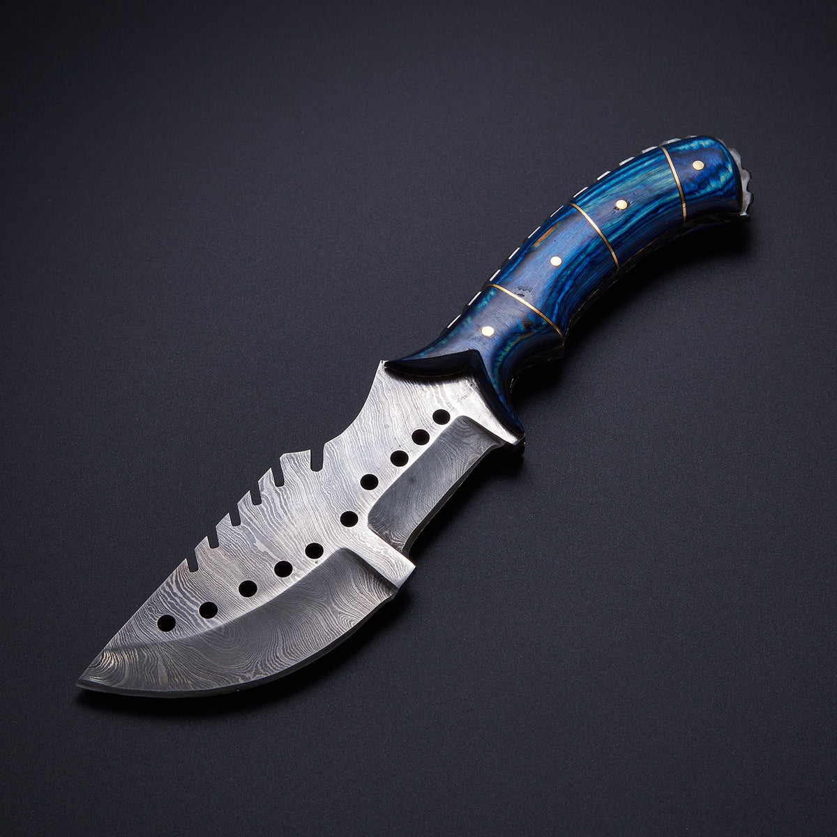 A custom handmade Damascus steel tracker knife with a blue hardwood handle and a leather sheath, displayed on a dark background.